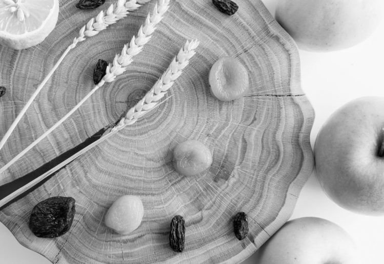 Elegant black and white still life featuring apples, lemon, wheat, and raisins on wood.