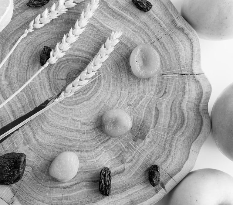 Elegant black and white still life featuring apples, lemon, wheat, and raisins on wood.
