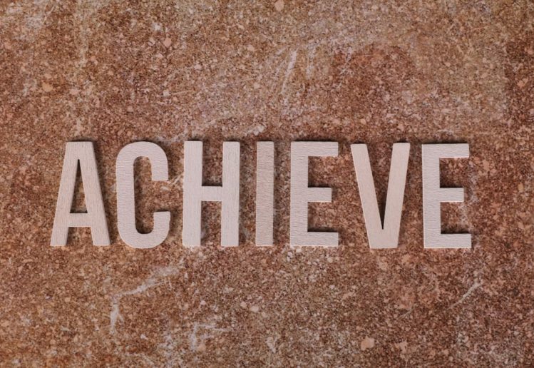 Wooden letters spelling 'ACHIEVE' on a textured brown surface, conveying motivation and success.