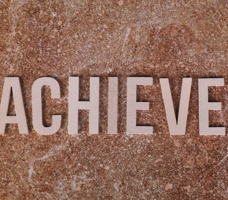 Wooden letters spelling 'ACHIEVE' on a textured brown surface, conveying motivation and success.